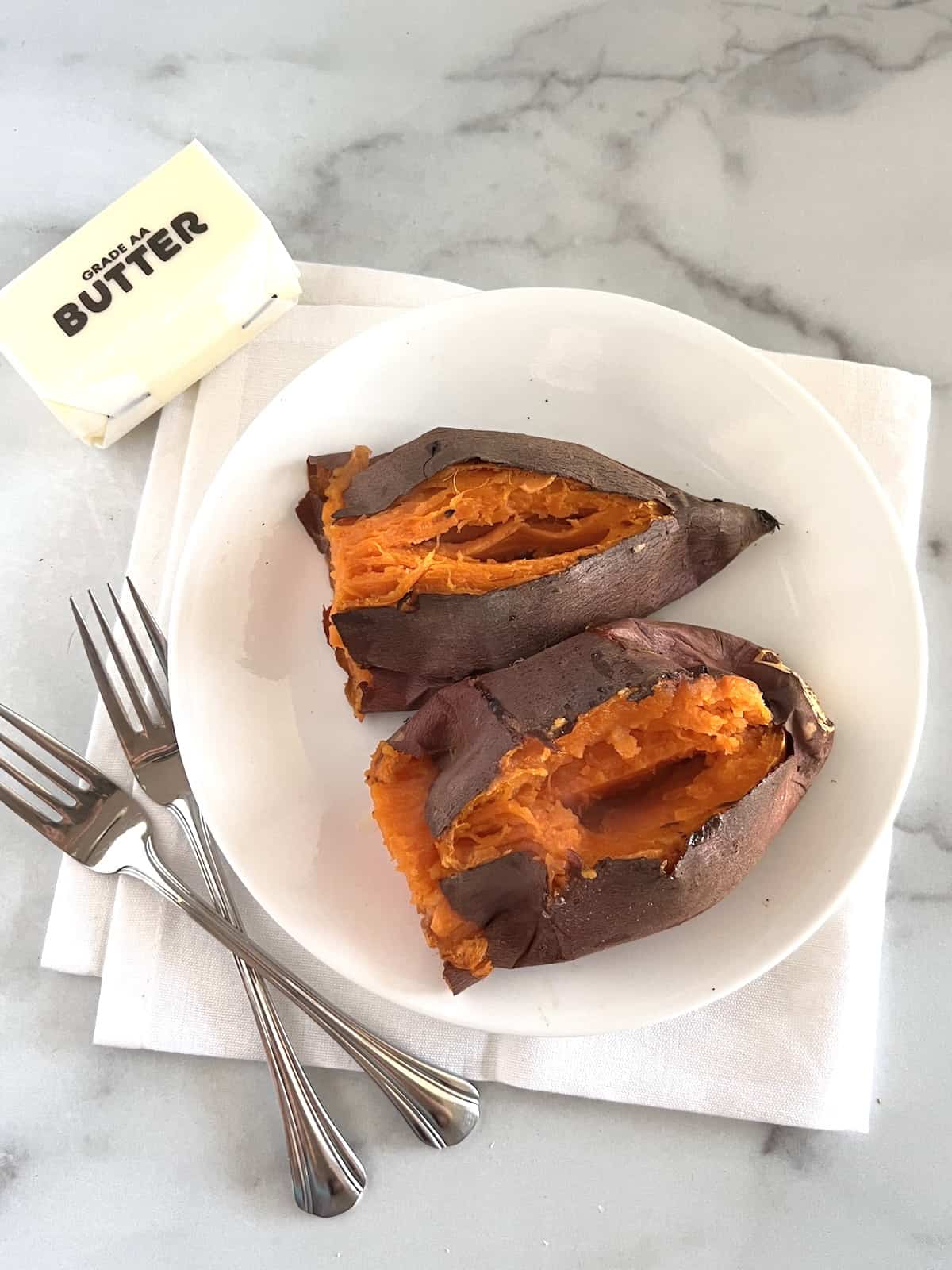 Air Fryer Baked Sweet Potatoes Split open on a plate with forks white linen napkin and stick of butterAir Fryer Baked Sweet Potatoes Split open on a plate with forks white linen napkin and stick of butter
