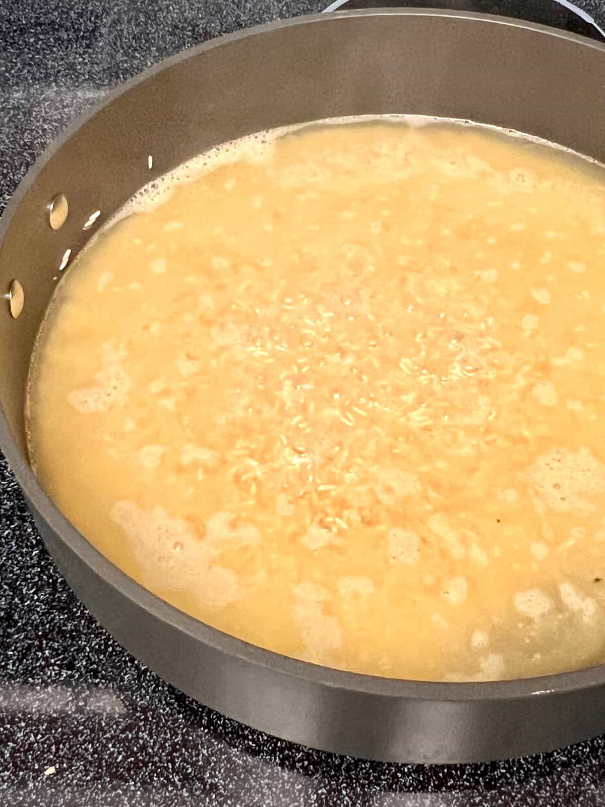 Chicken broth simmering in the pan with toasted rice.