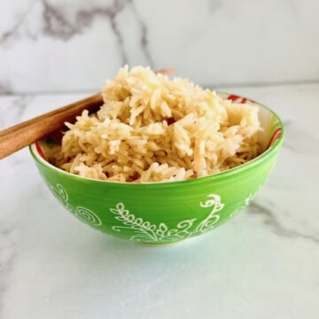 Bowl with long grain rice with broth piled high and chopsticks resting on the edge.