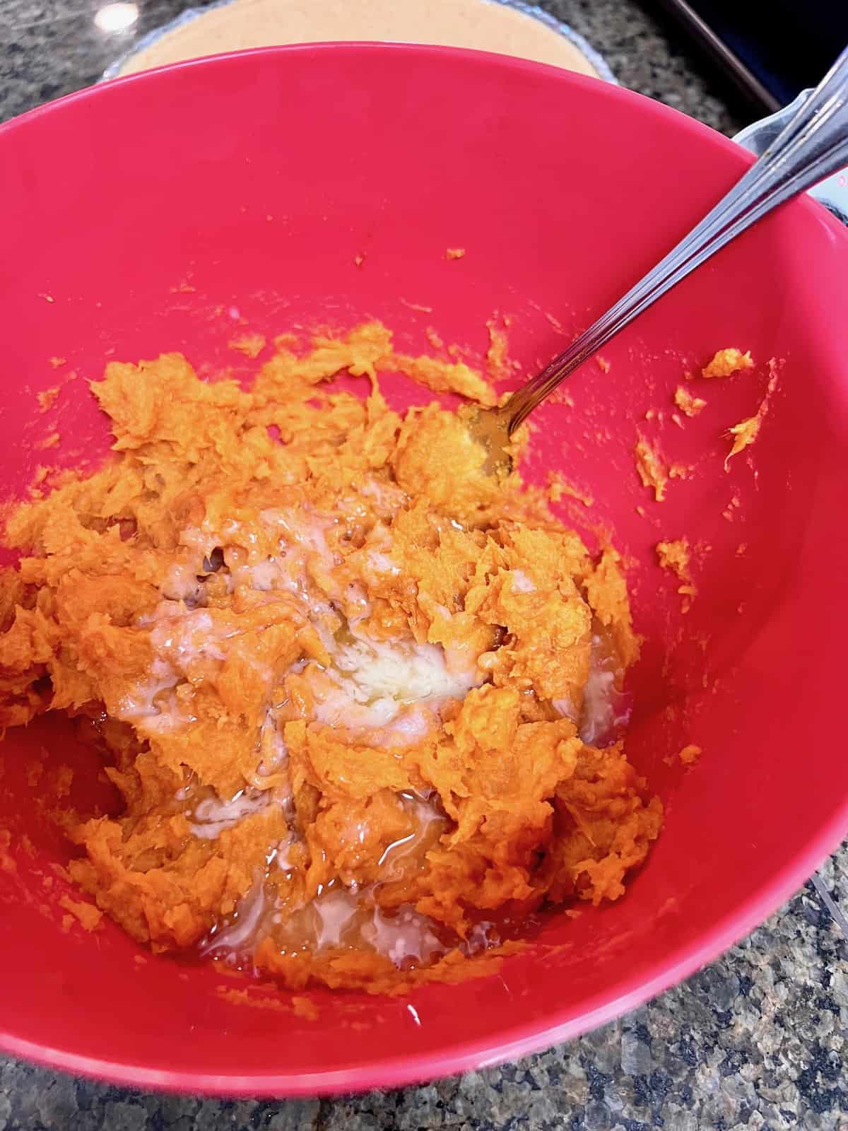 Melted butter added to a bowl of smashed baked sweet potatoes.