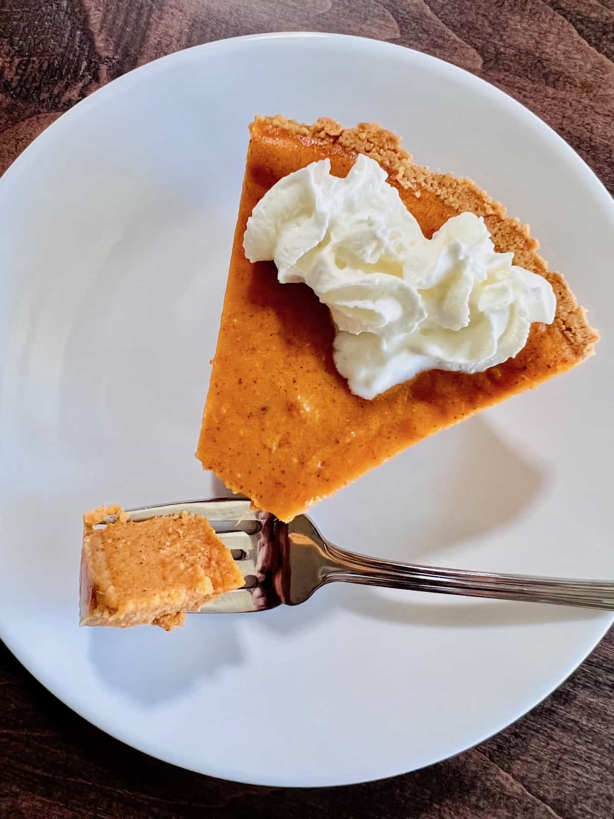 Graham Cracker Crust Sweet Potato Pie On a plate with a fork holding a bite.