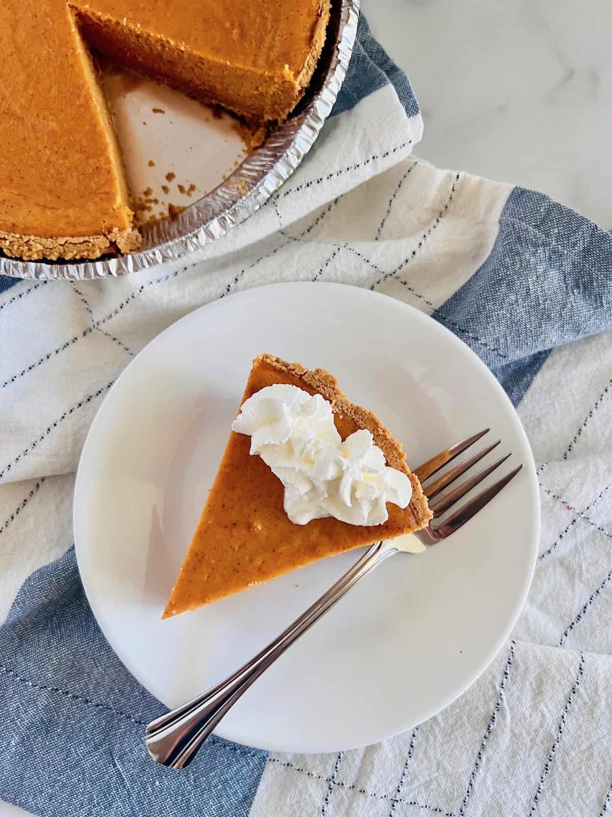 Graham Cracker Crust Sweet Potato Pie Plated slice with a dollop of whipped cream near whole pie on linen napkin