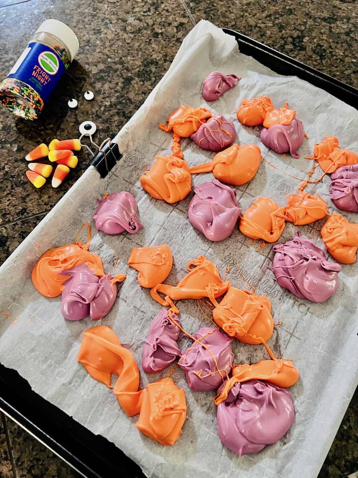 Blobs of orange and purple candy melted on a parchment sheet.
