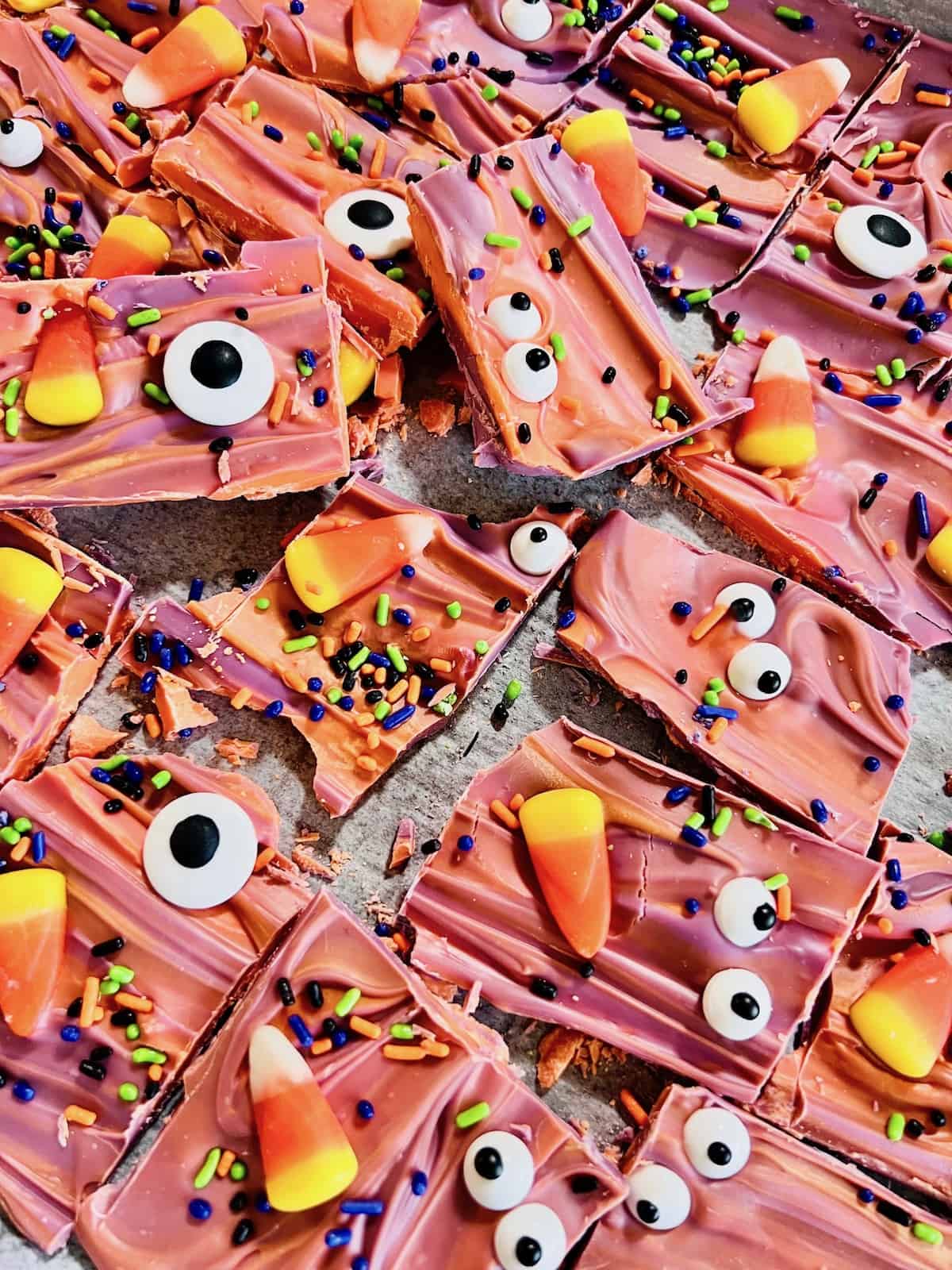 Broken pieces of Halloween Candy Bark topped with colorful sprinkles candy corn and candy eyes.
