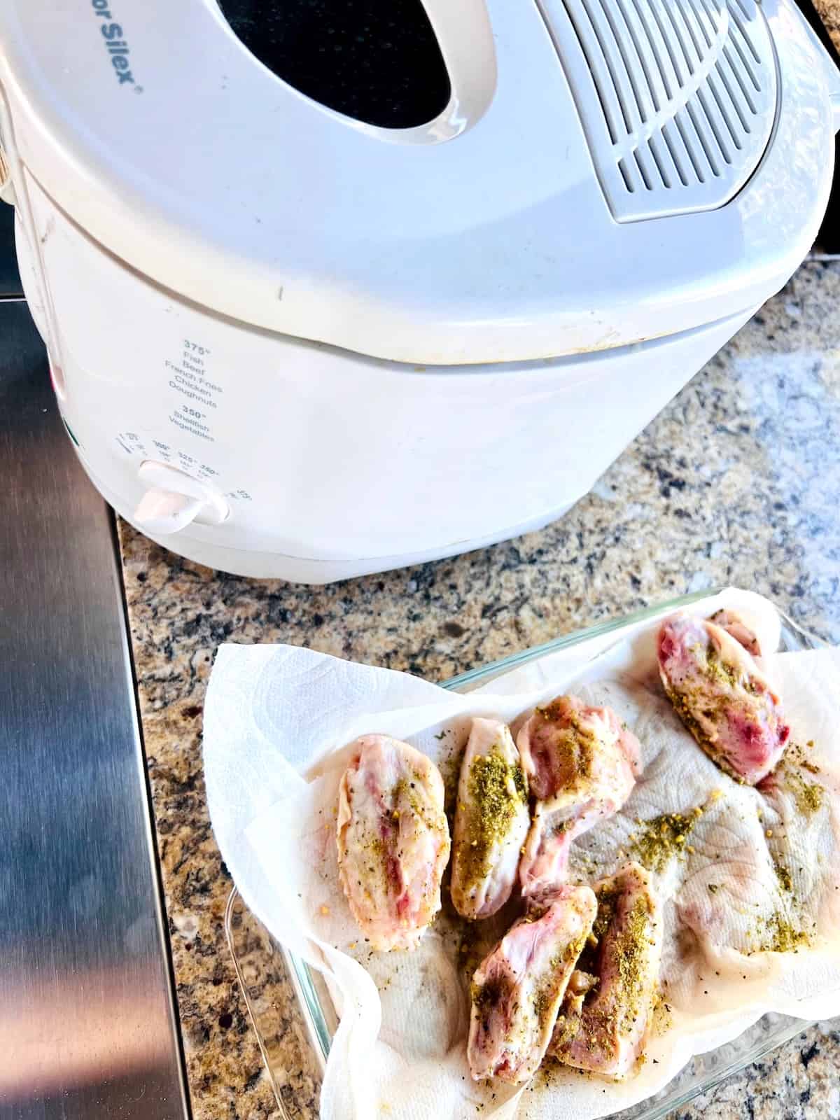 Dish with raw wings next to the deep fryer.