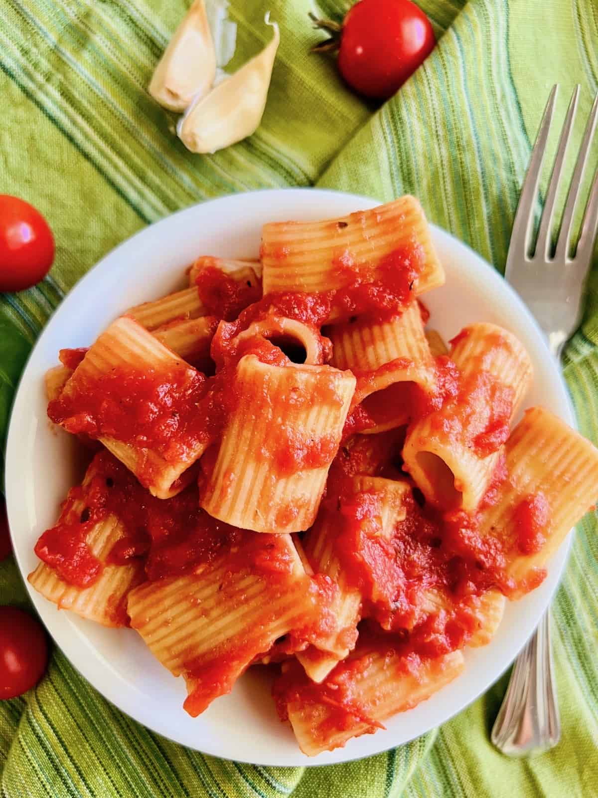 Pasta alla Pizzaiola In a bowl covered in sauce next to a spoon and cherry tomatoes