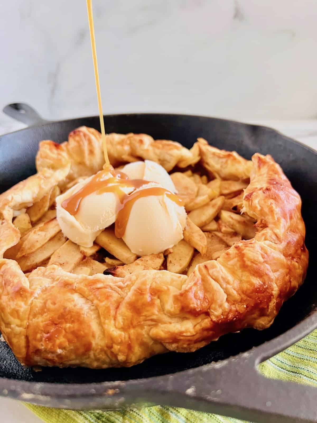 Caramel sauce pouring down over ice cream and apple galette in a cast iron skillet.