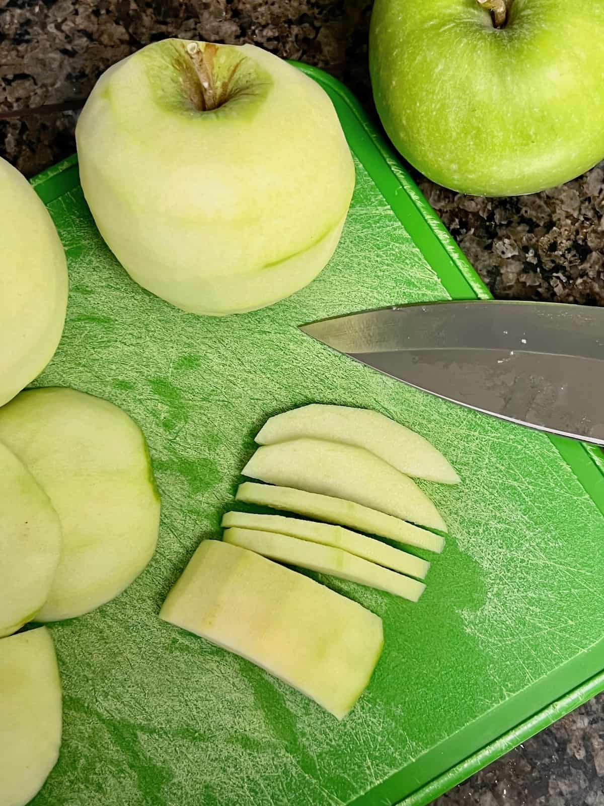 Peeled apples and one in slices on a cutting board.