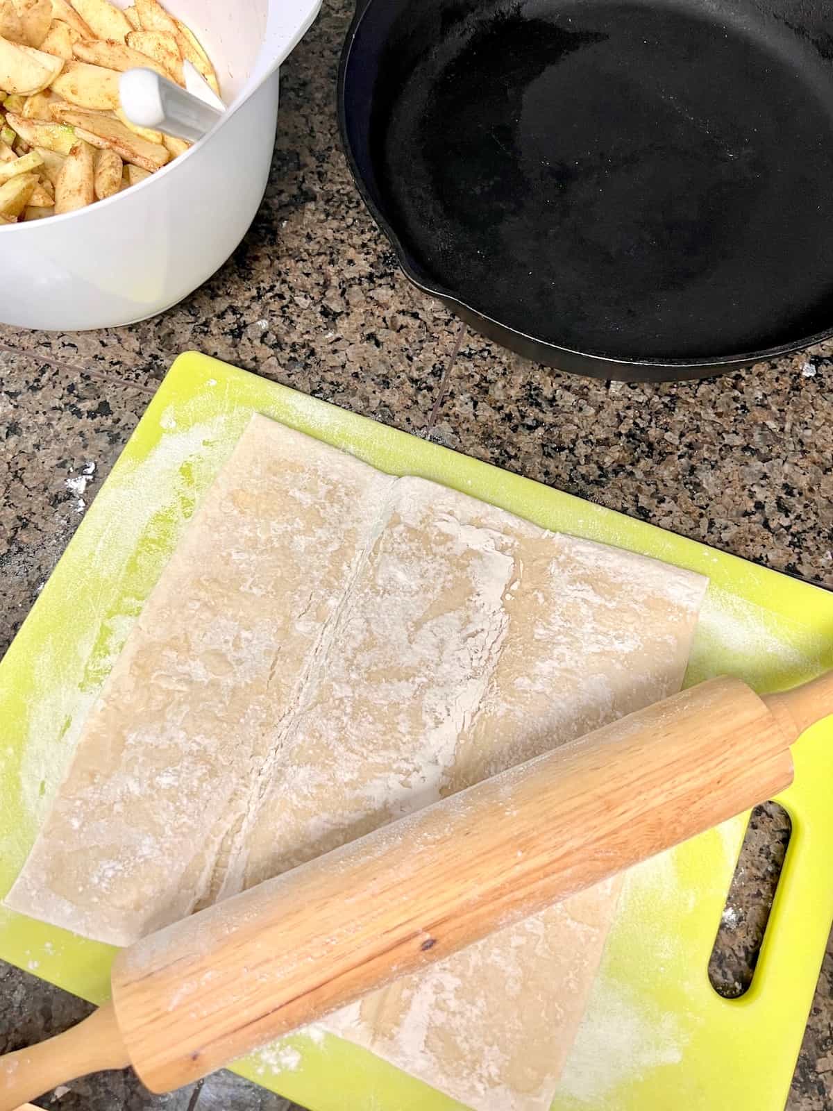 Unfolded puff pastry on a cutting board with a rolling pin.