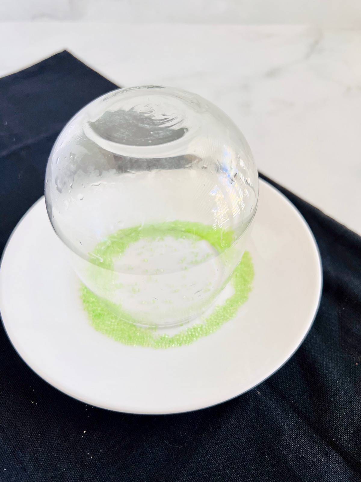 Glass upside down in a dish of green sugar sprinkles.