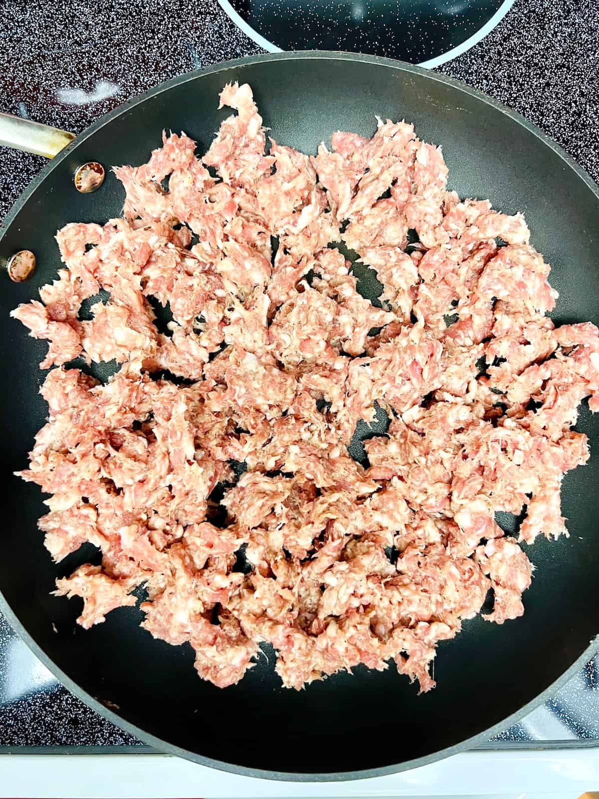 Crumbles of raw sausage in a large skillet on the stove.