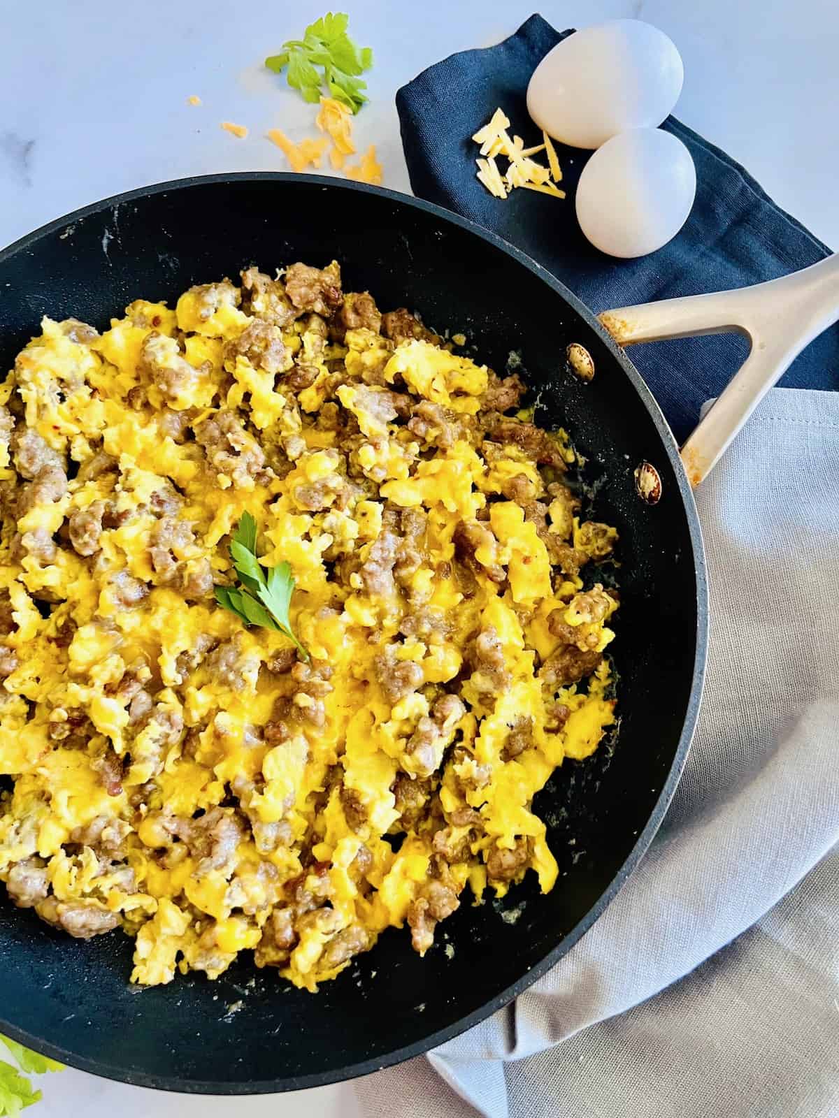 https://theshortordercook.com/wp-content/uploads/2023/11/Breakfast-Sausage-Egg-Cheese-Scramble-in-a-skillet-topped-with-parsley-leaves-next-to-eggs-in-the-shell-and-shredded-cheese.jpg