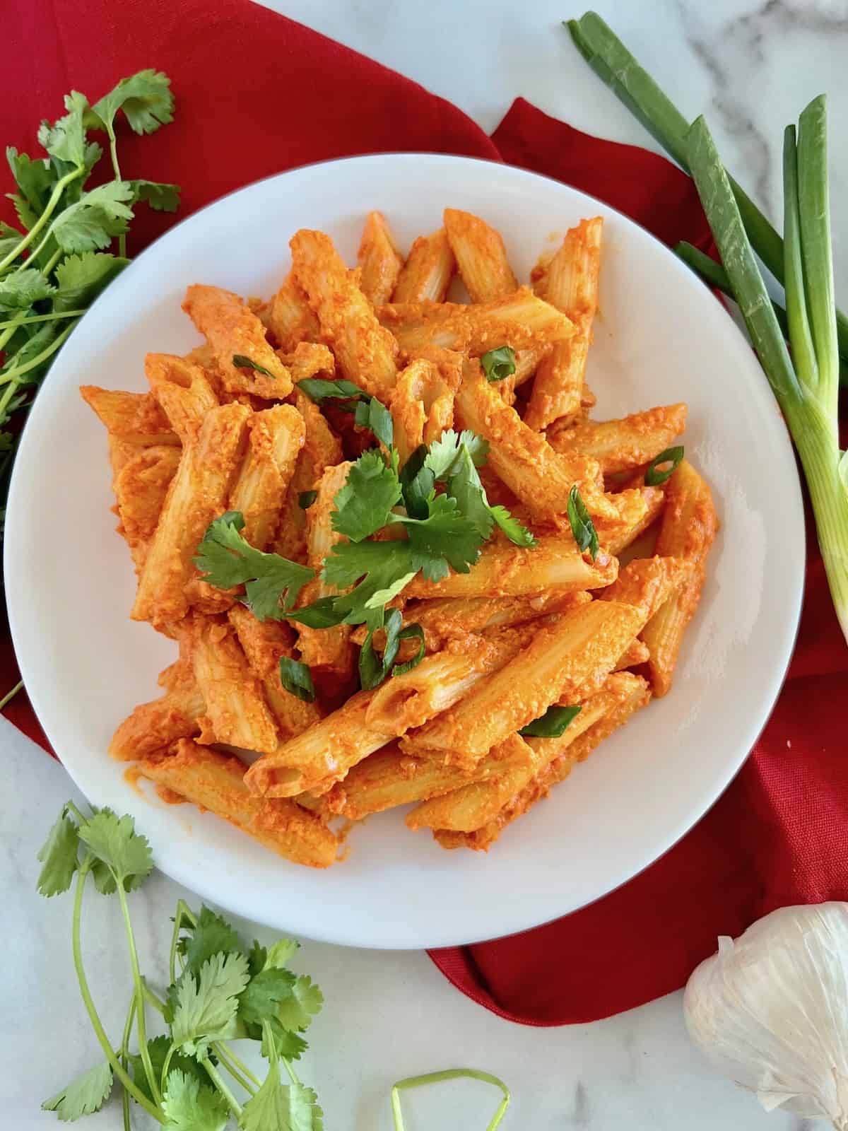 Gochujang Pasta Piled on a plate with cilantro and green onions next to bulb of garlic and red linen napkin.