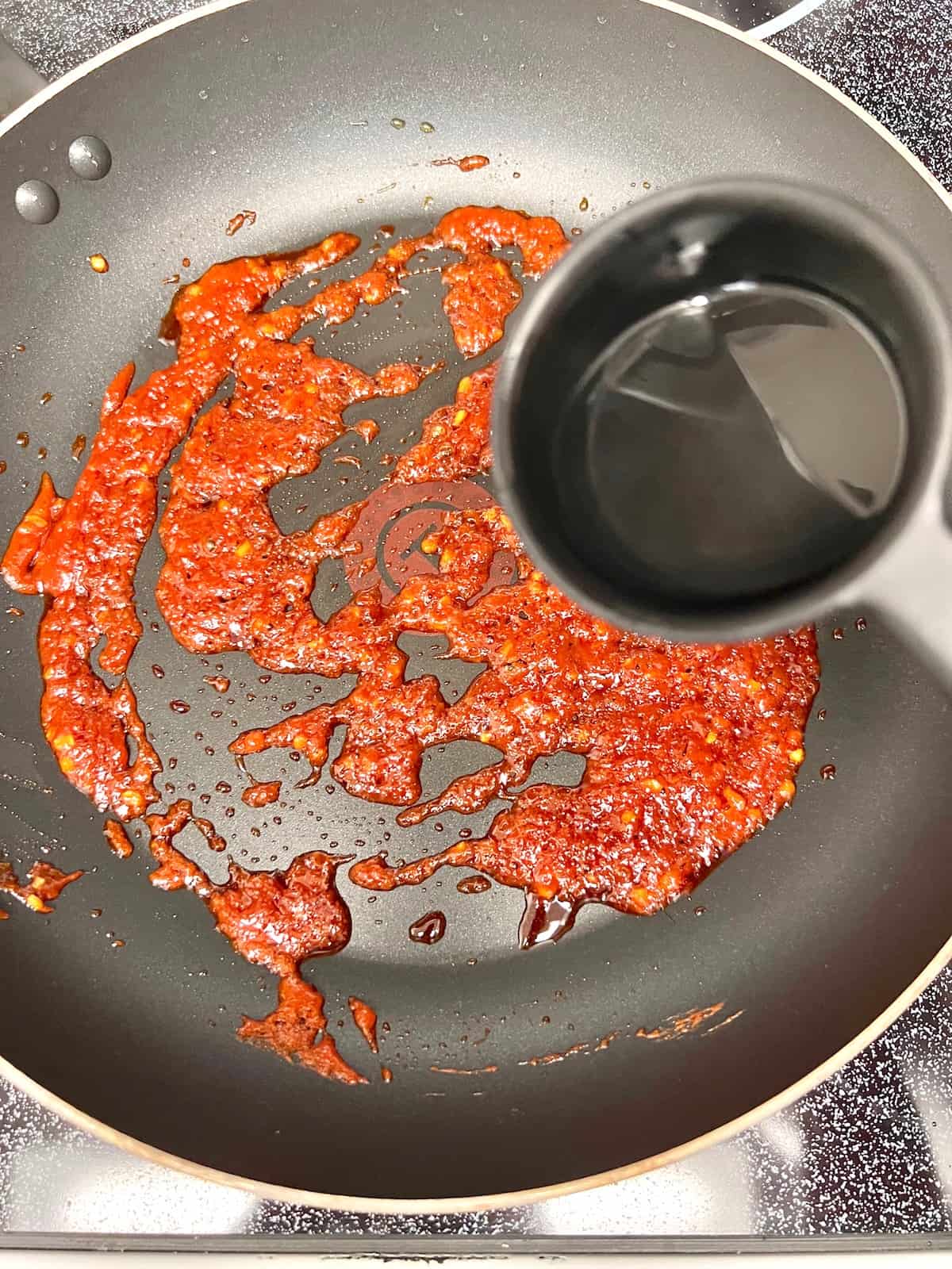 Pouring pasta water into the pan with garlic and gochujang.