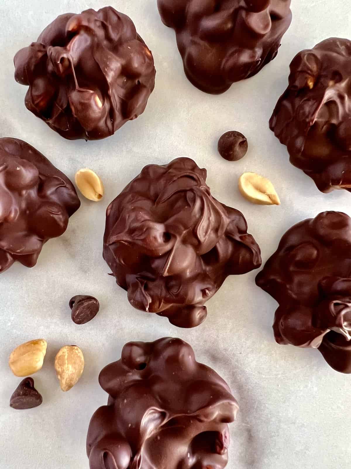 Chocolate Peanut Clusters Set on parchment with chocolate chips and peanuts scattered