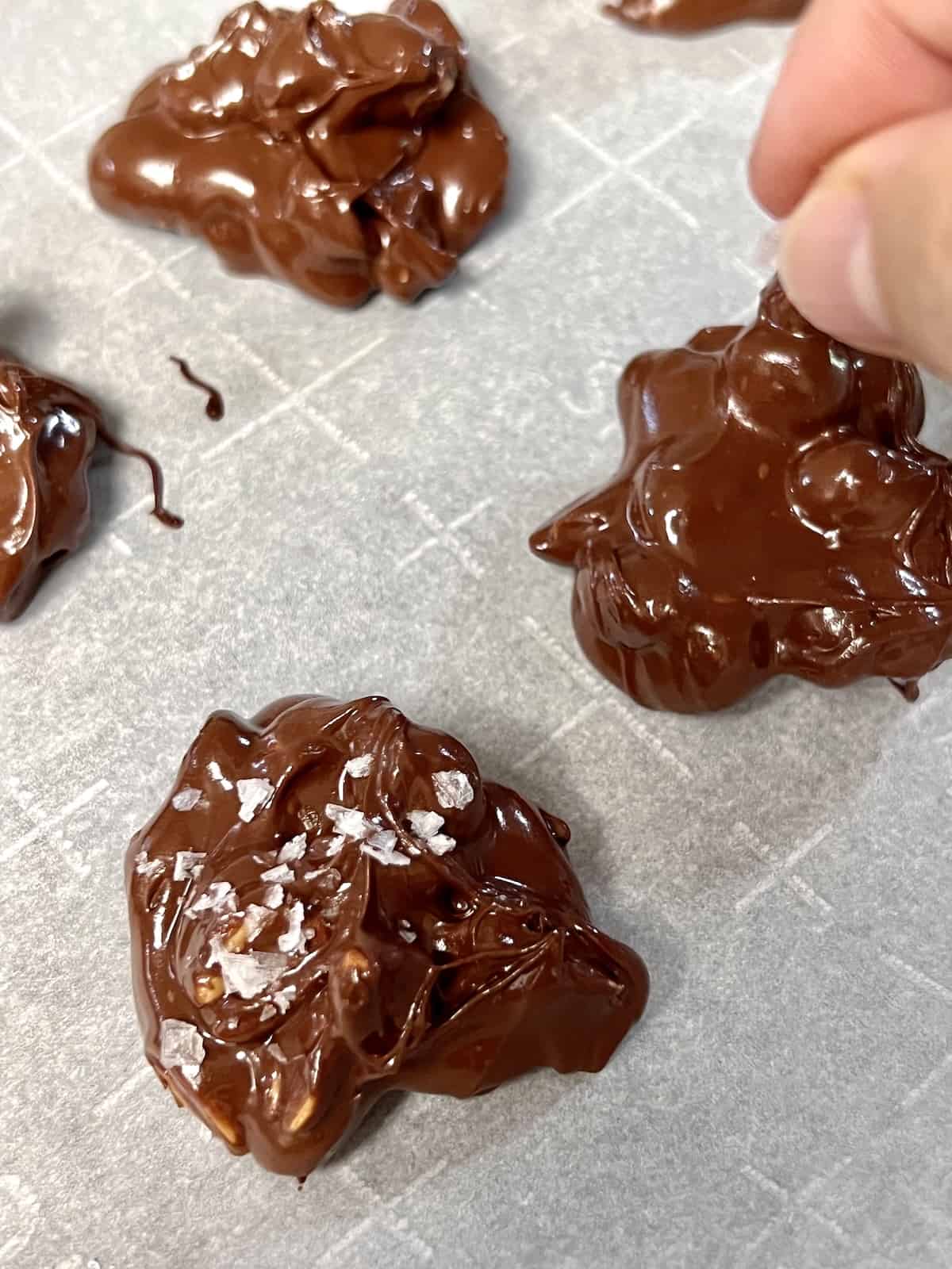 Chocolate Peanut Clusters Sprinkling flaky sea salt on top of chocolate peanut clusters