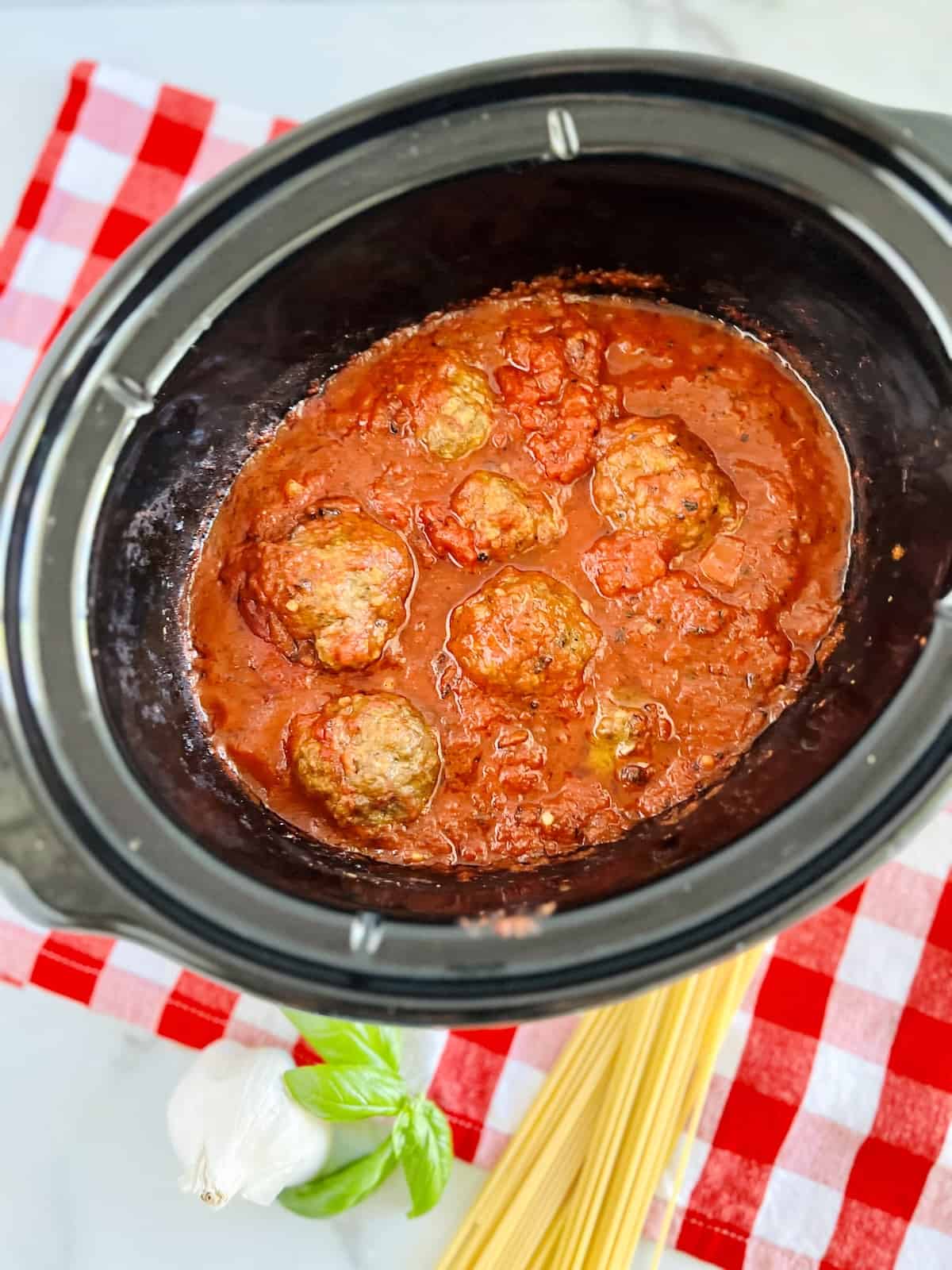 Slow Cooker Italian Meatballs & Sauce  in crockpot with basil garlic and spaghetti on the side