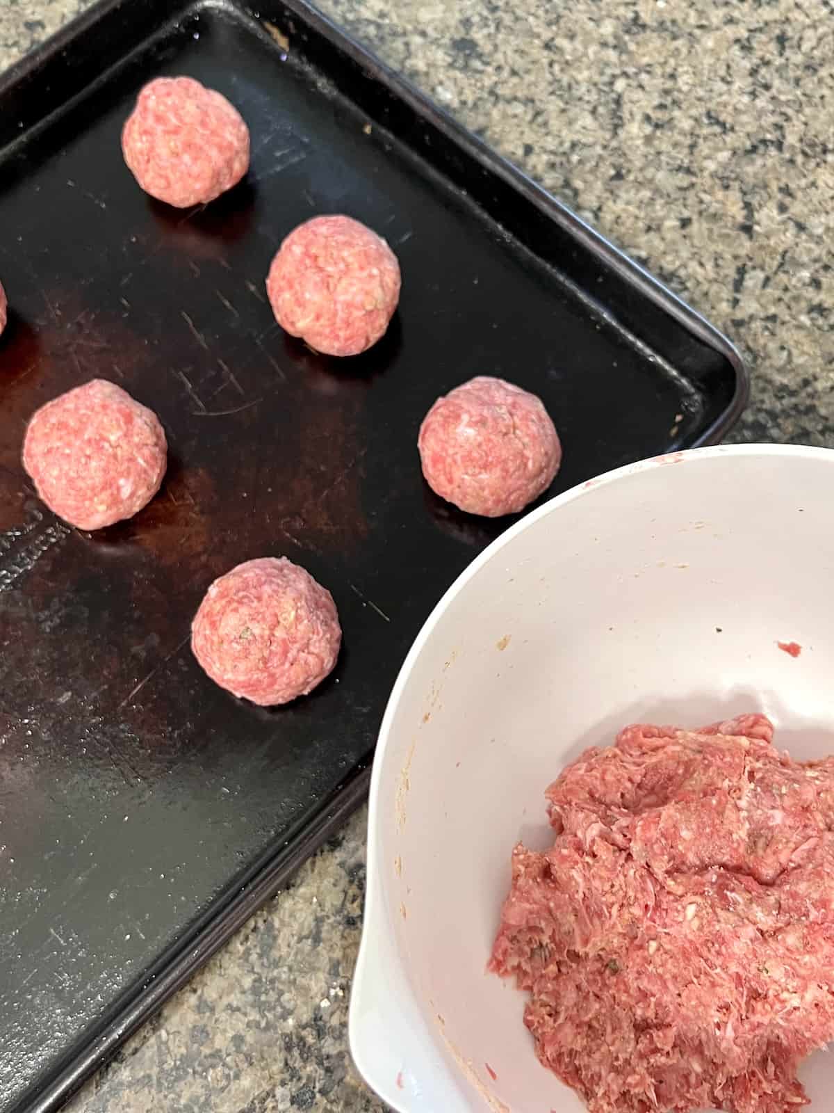 Slow Cooker Italian Meatballs & Sauce Rolled meatballs on the sheet pan next to bowl filled with beef mixture.