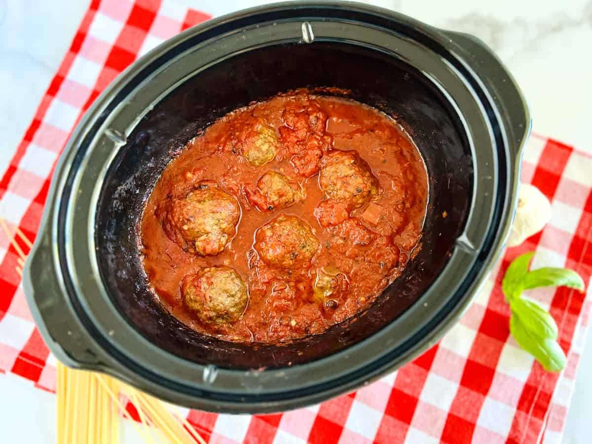 Crockpot filled with red sauce and round meatballs.