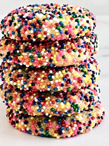 Sprinkle Sugar Cookies covered in rainbow colored nonpareils stacked.