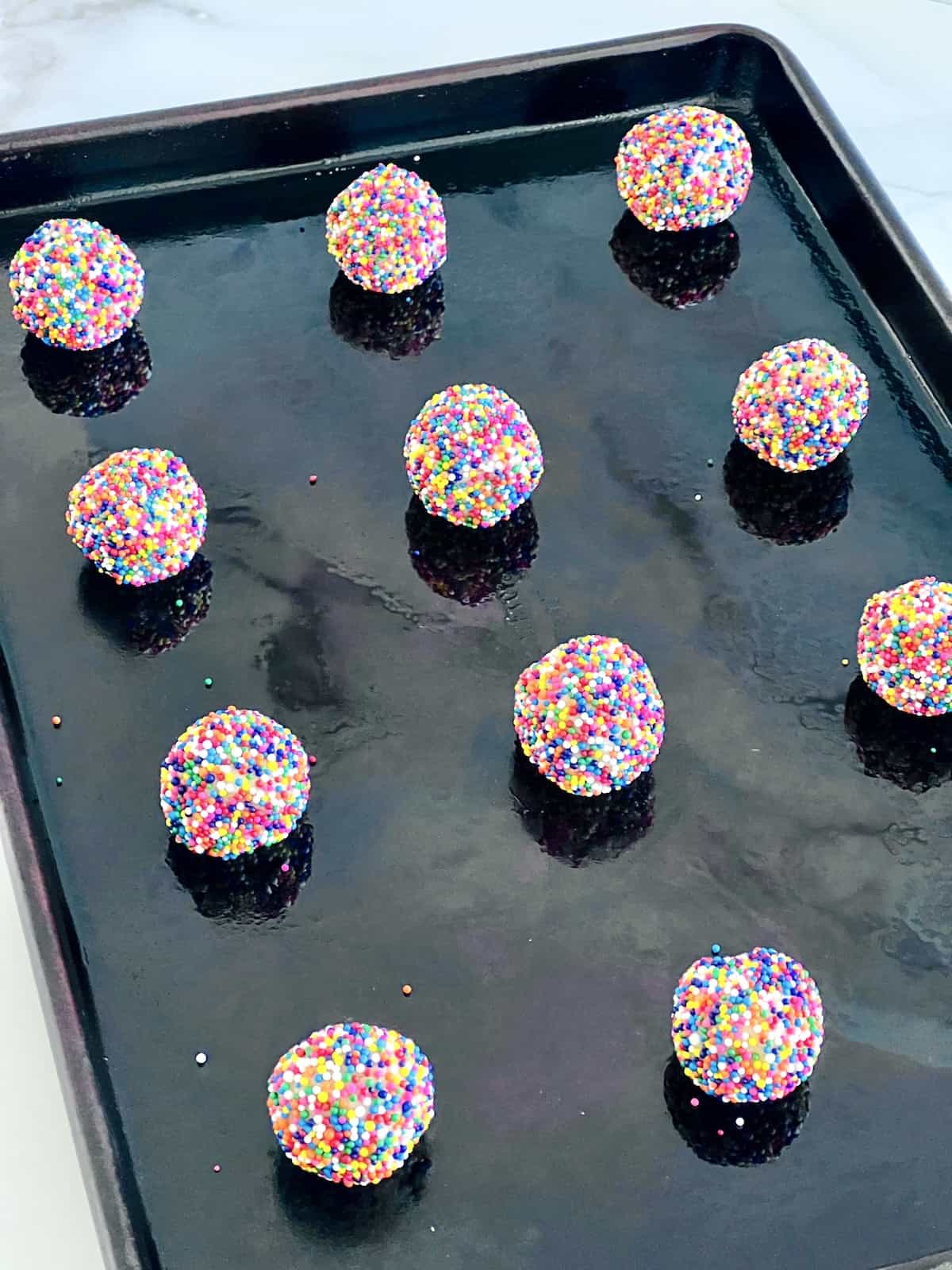 Rolled sugar cookie dough covered in nonpareils on the baking sheet.