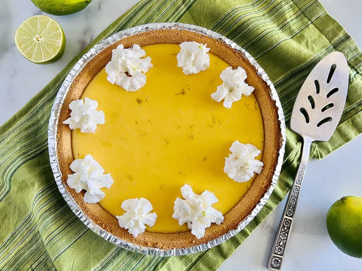 Easy 4- Ingredient Key Lime Pie Landscape whole pie topped with dollops of whipped cream.