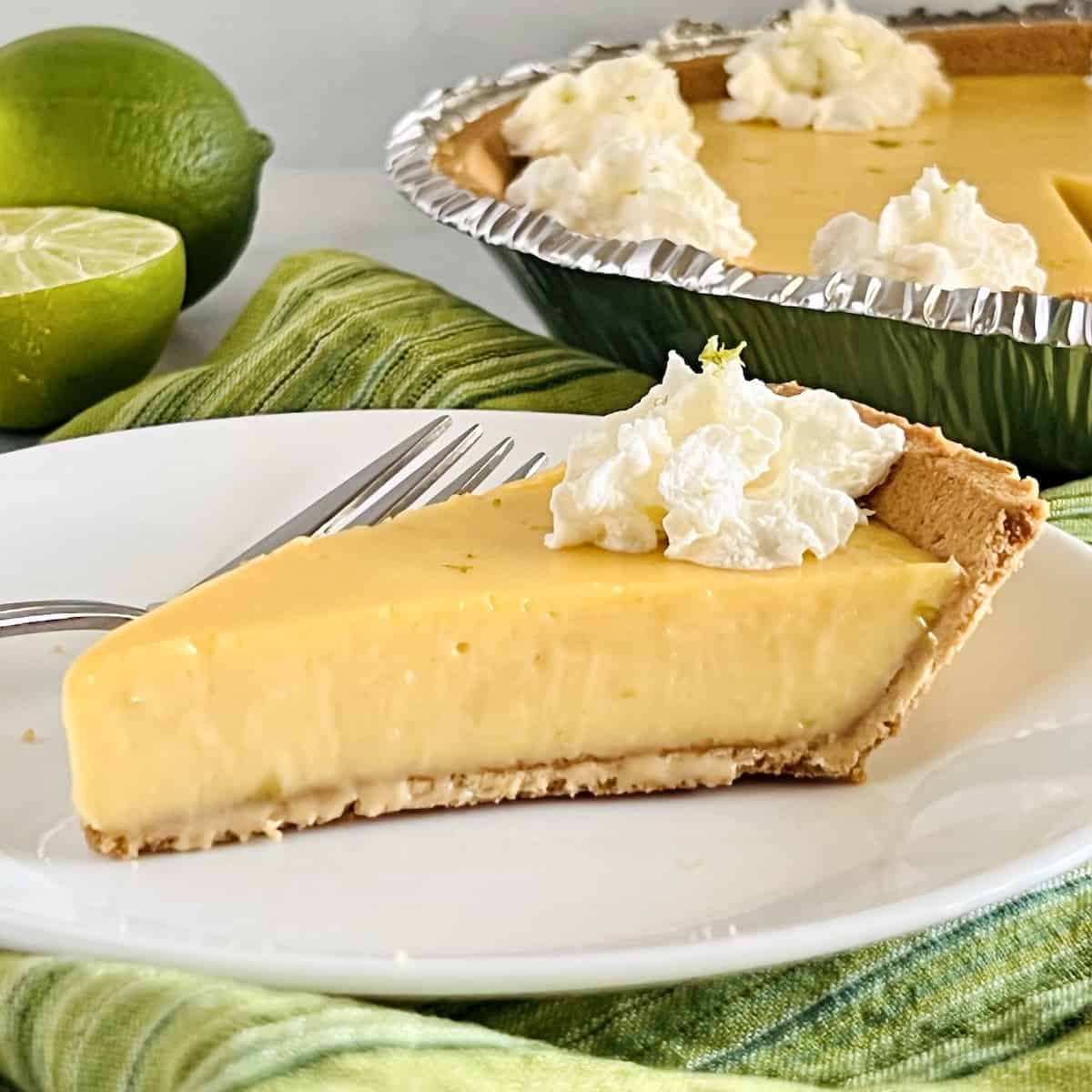 Graham cracker crust filled with key lime pie filling and topped with whipped cream on a plate with a fork.