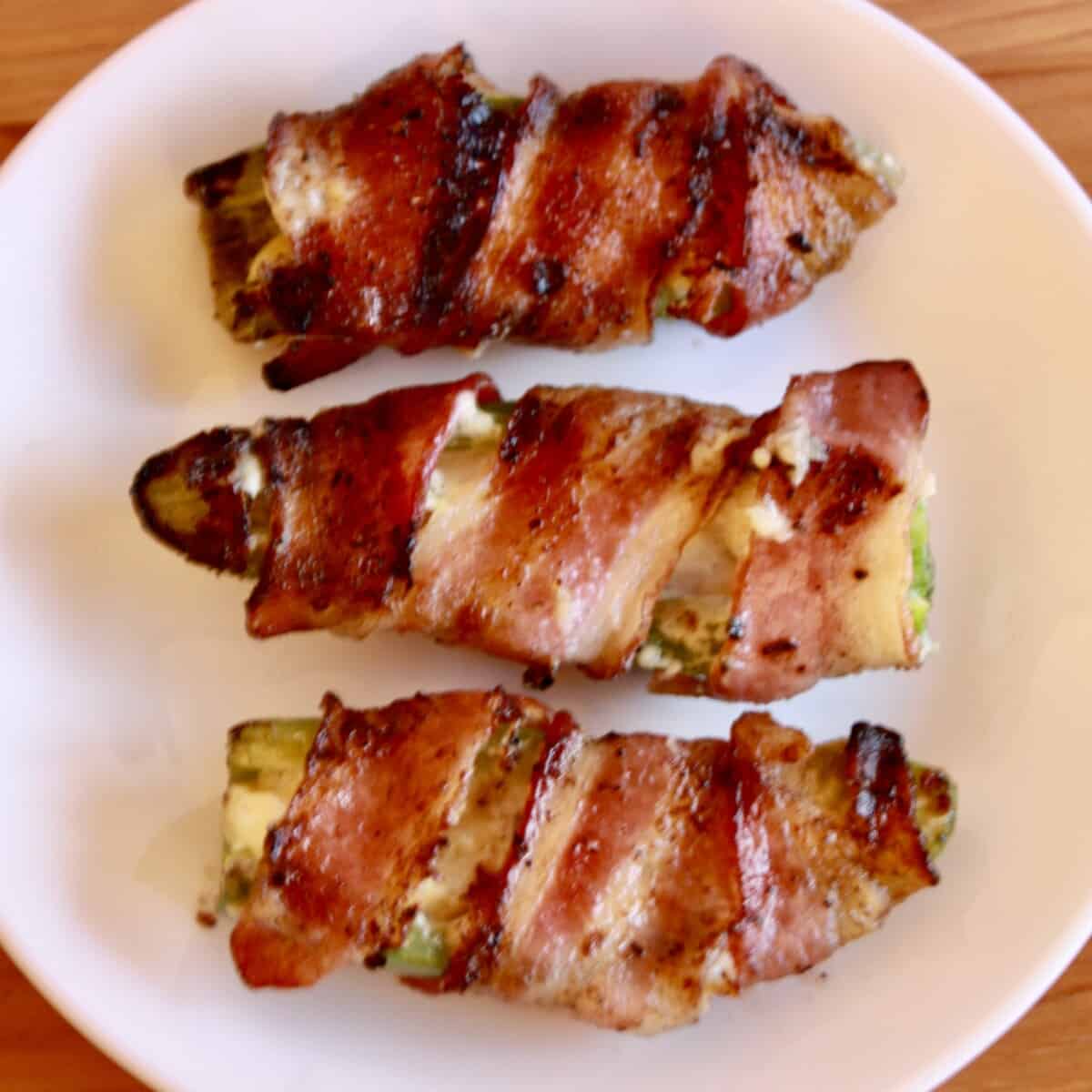 Grilled Jalapeño Poppers wrapped in crispy bacon on a plate.