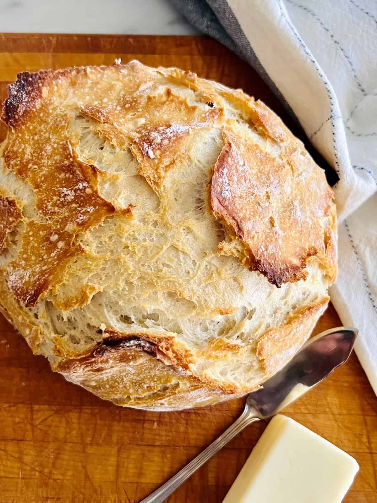 Dutch Oven No Knead Bread Best recipe for round white bread loaf on cutting board with butter.