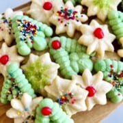 Board covered in a stack of colorful Spritz Cookies in the shapes of green Christmas trees and white snowflakes with sprinkles.