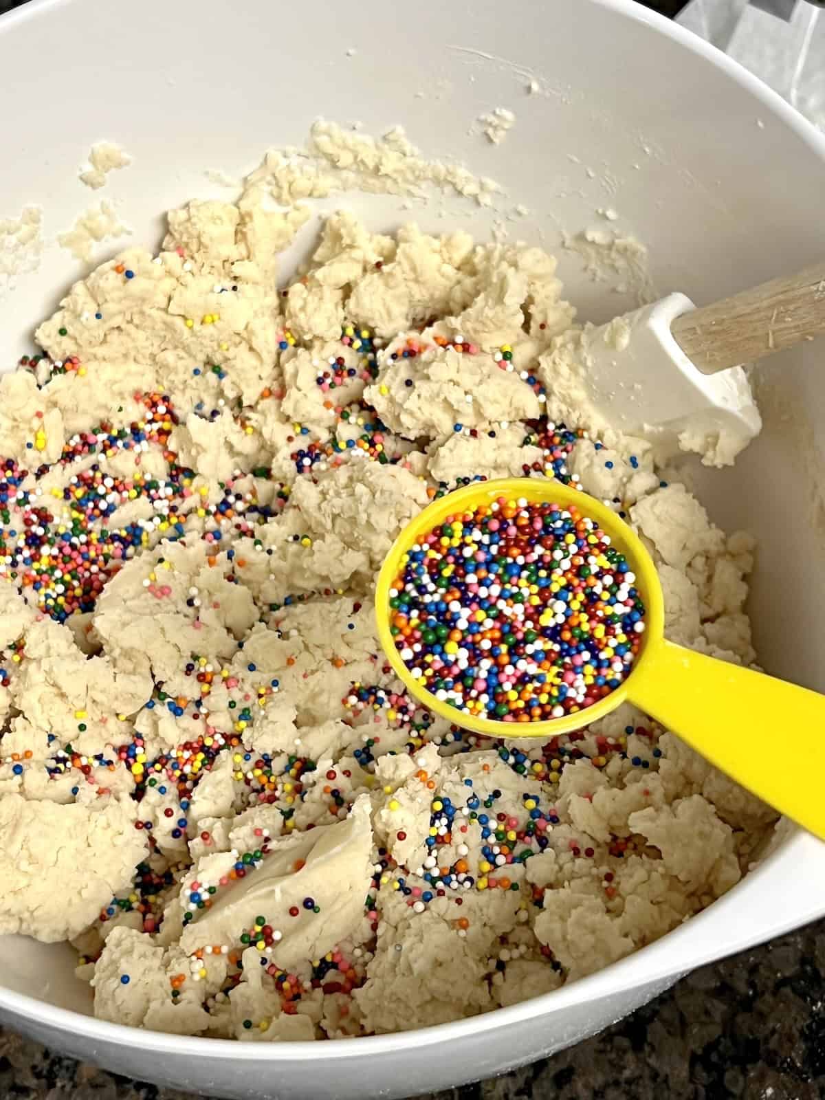 Adding rainbow nonpareils to shortbread cookie dough.