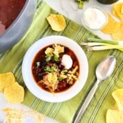 Easy Black Bean Enchilada Soup in a bowl topped with cheese, sour cream, cilantro & tortilla chips.