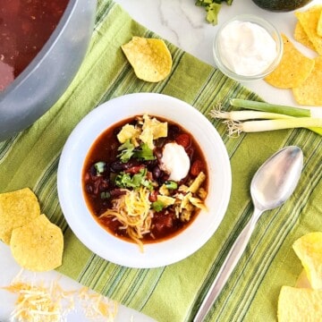 Easy Black Bean Enchilada Soup in a bowl topped with cheese, sour cream, cilantro & tortilla chips.