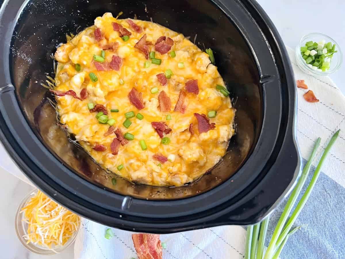 CrockPot Loaded Chicken & Cauliflower Casserole in the slow cooker topped with melted cheddar jack cheese & bacon.