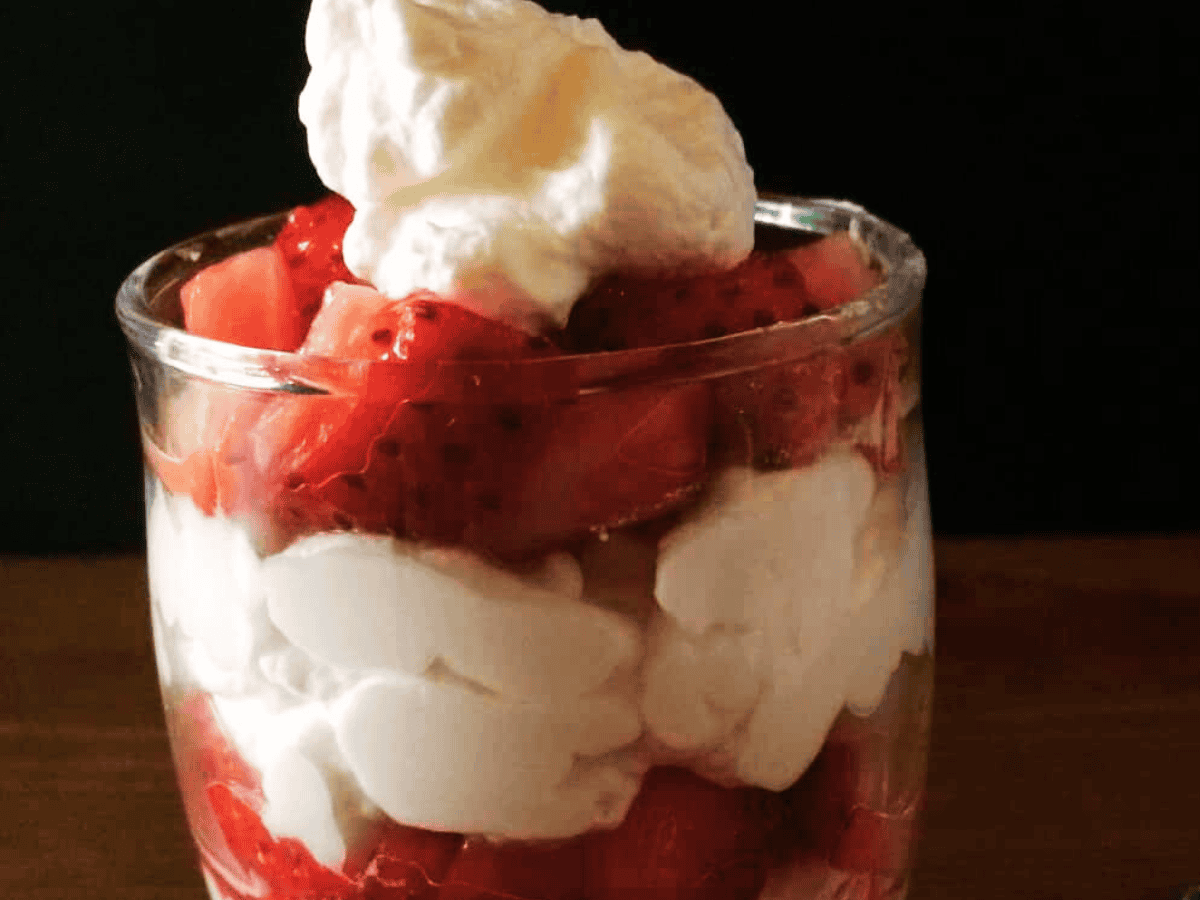 Glass jar with layers of diced fresh strawberries and fresh whipped cream.
