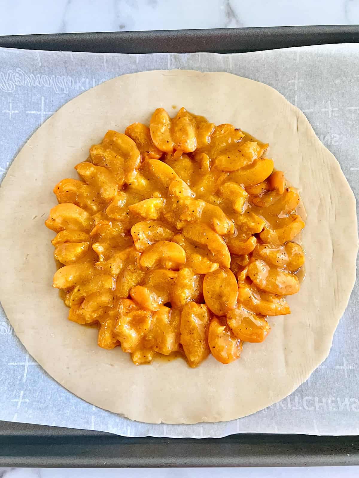Easy Apricot Galette Quartered apricots in a design in the middle of round pie crust on baking sheet.