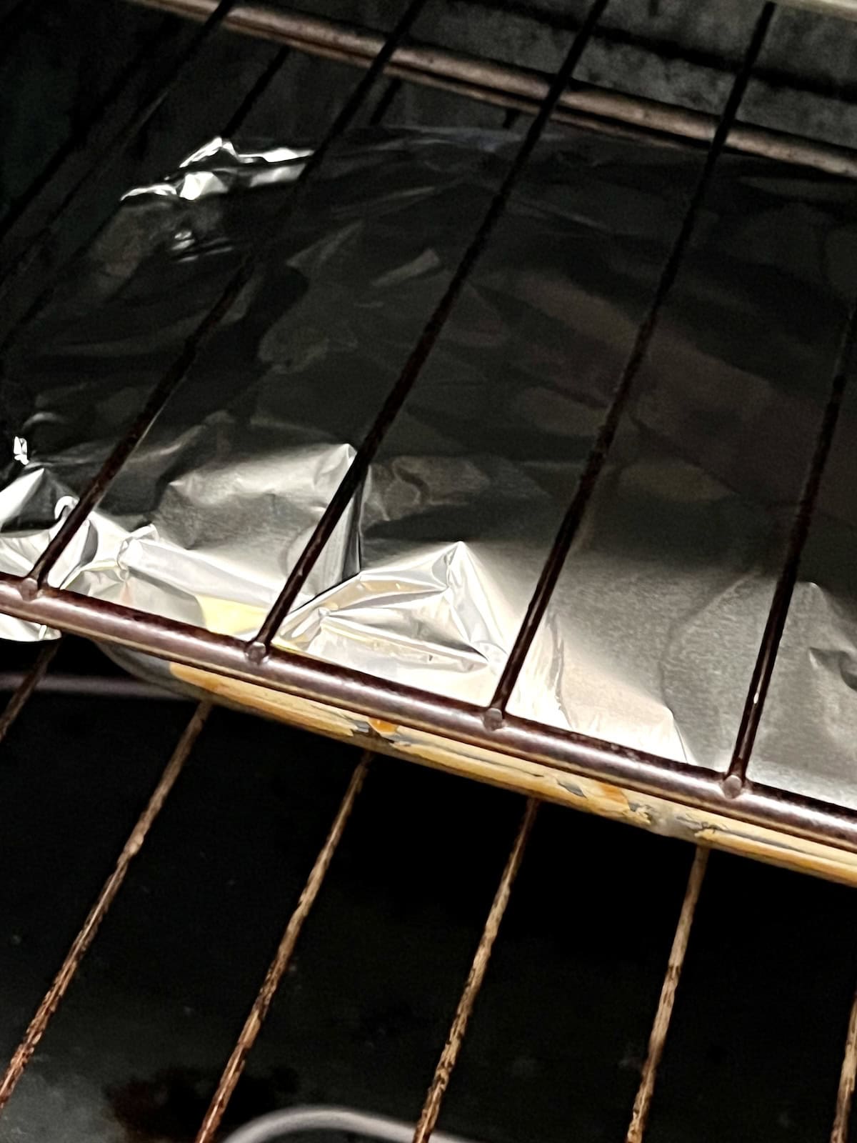 Baking dish of sliders covered in foil in the oven.
