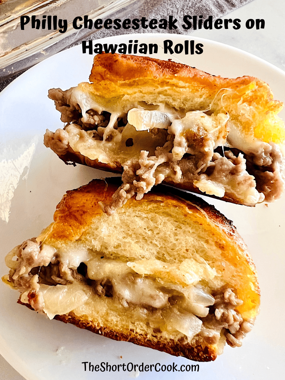 Two hawaiian rolls filled with cheese, steak, & onions on a plate.