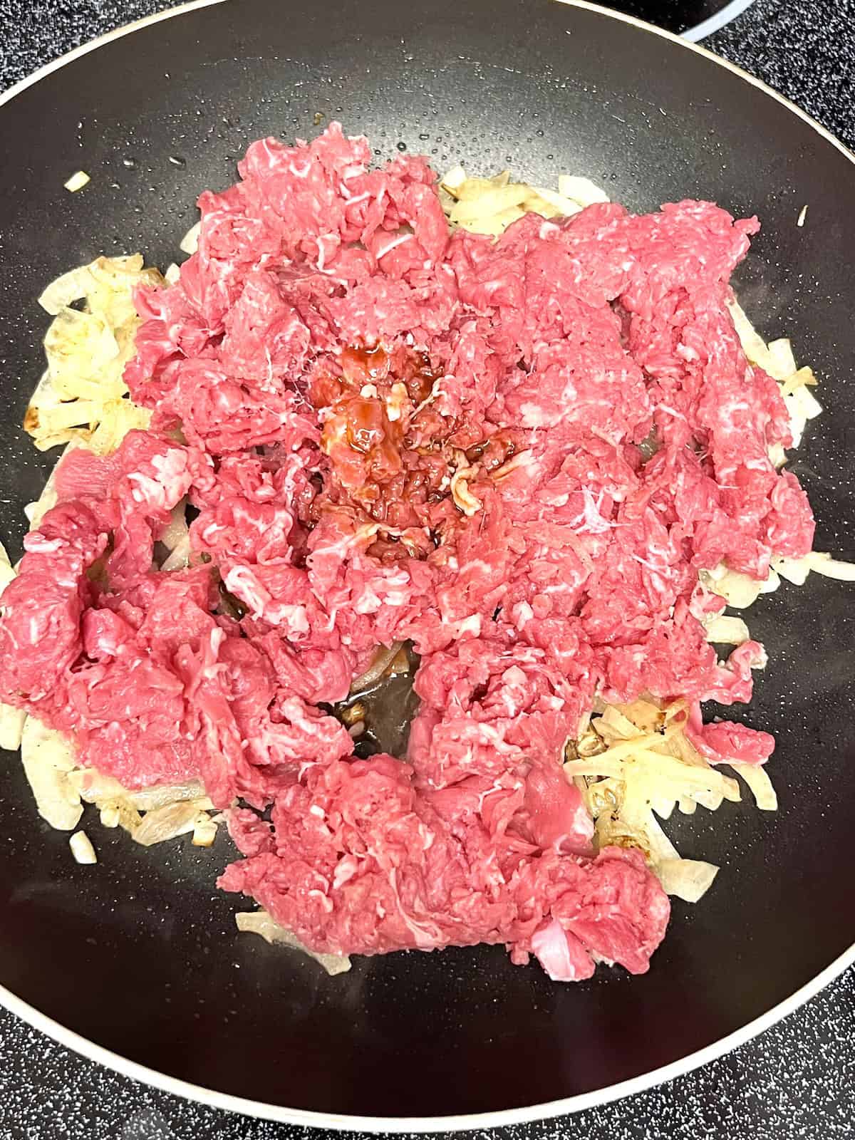 Pan with cooked onions raw shaved beef and spices.
