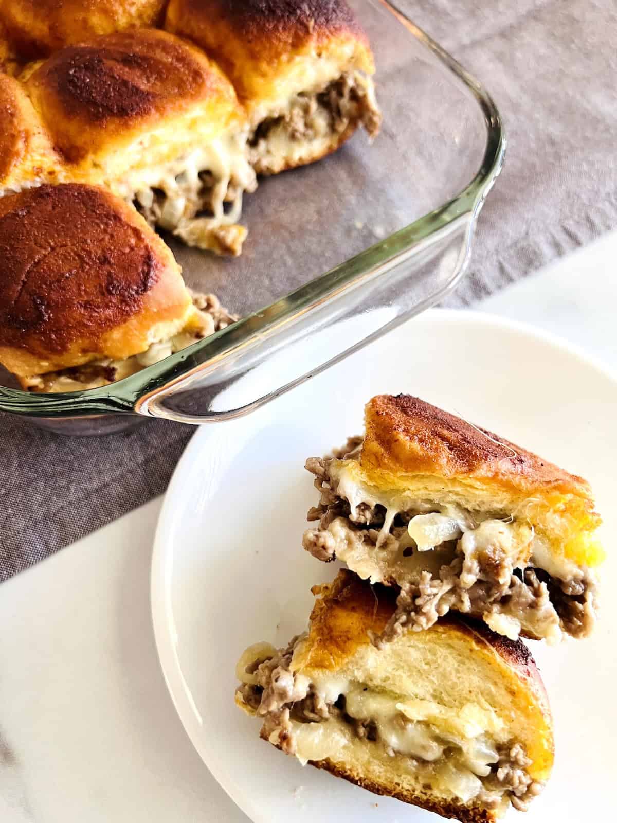 Philly Cheesesteak Sliders on Hawaiian Rolls Plate with two cheesesteak sliders next to pan with the rest.