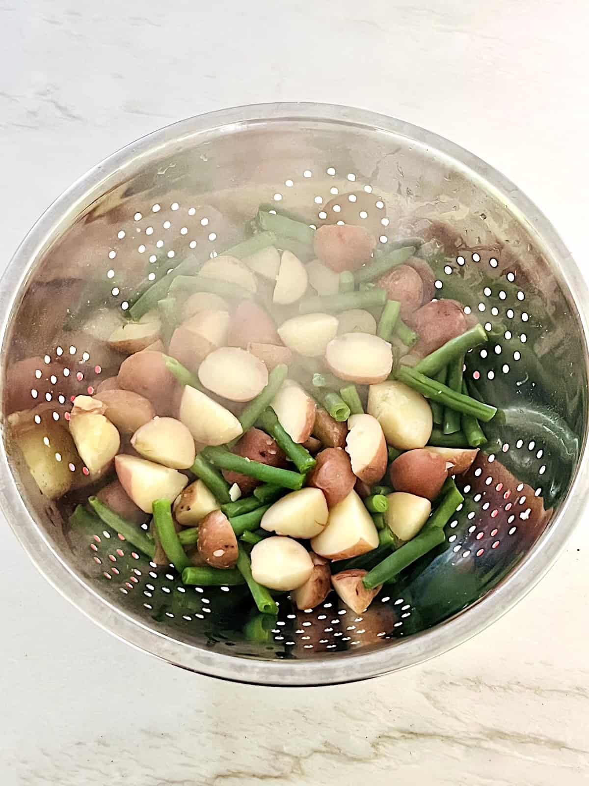 Colander with cooked red potatoes and string beans.