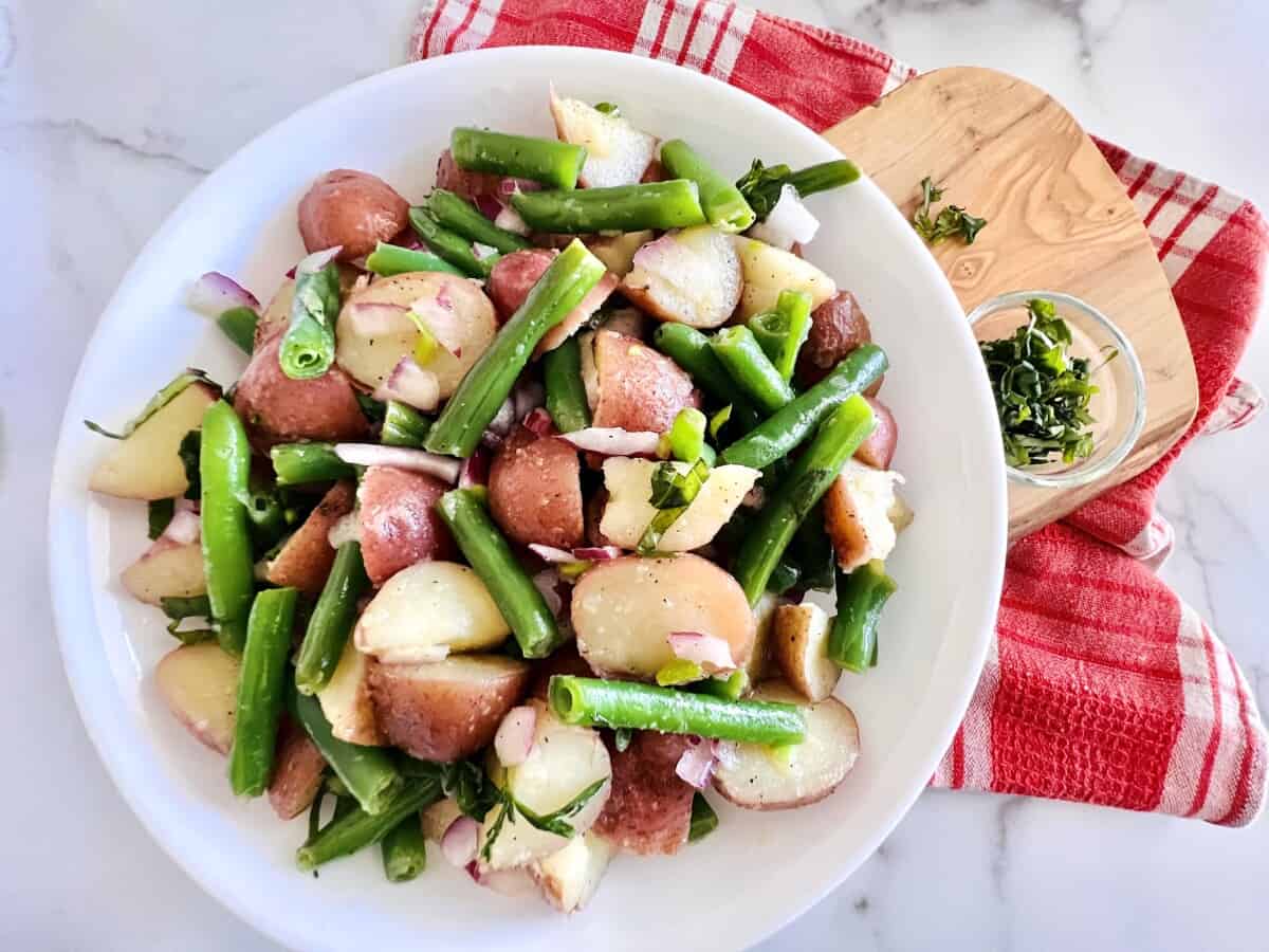 Italian Green Bean and Potato Salad in a serving bowl next to a bowl with fresh herbs for topping. 