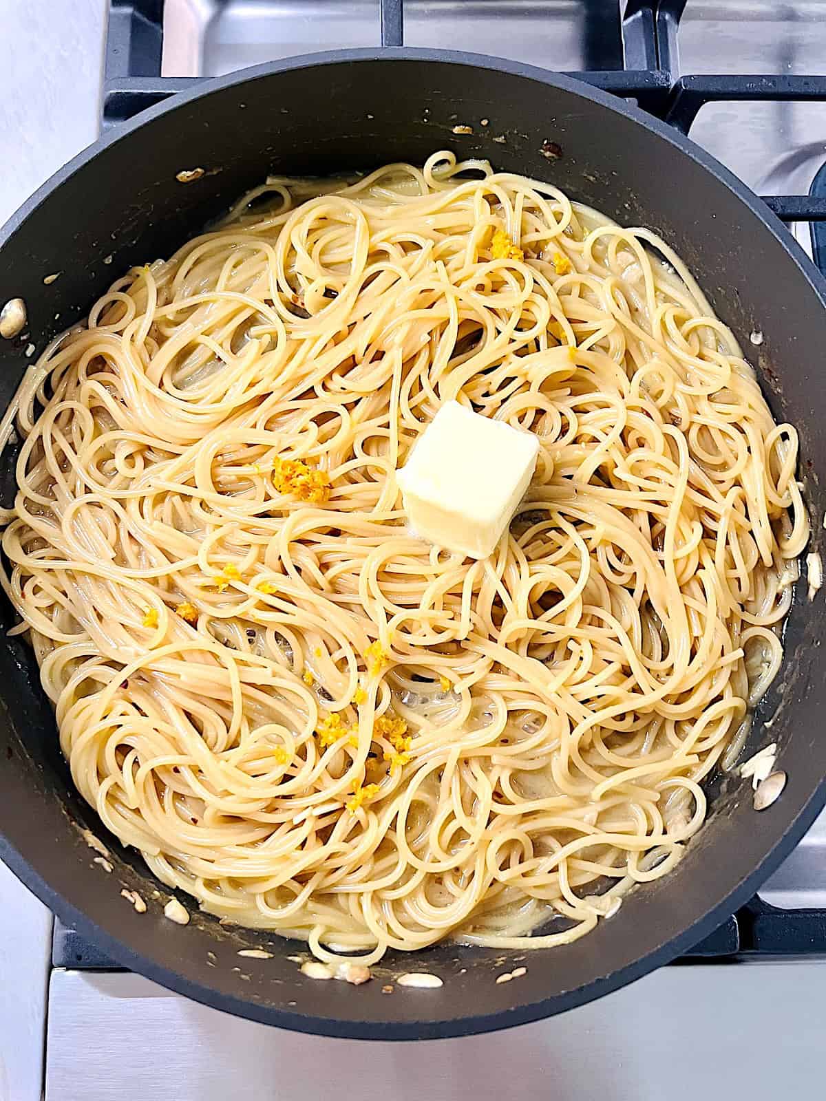 Adding butter and lemon zest to cooked spaghetti.