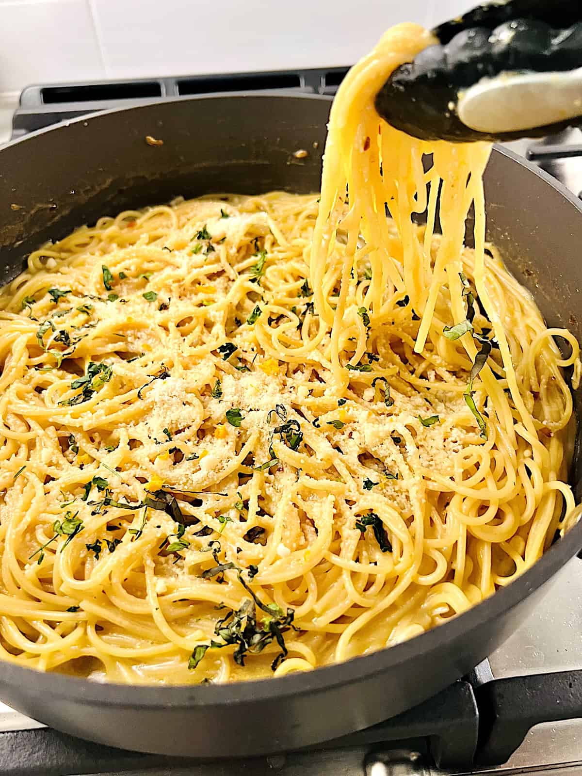 One Pot Lemon Butter Pasta (Pasta al Limone) Ready with tongs grabbing some from the pot.