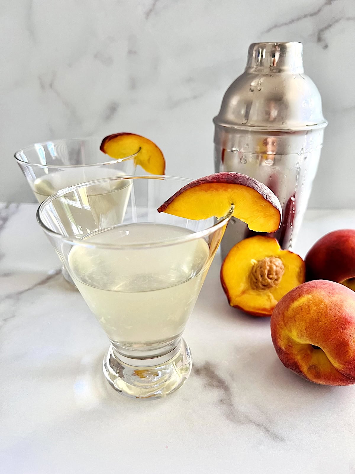 Peach Martini Served up in martini glasses next to peaches and garnished with peach slices.