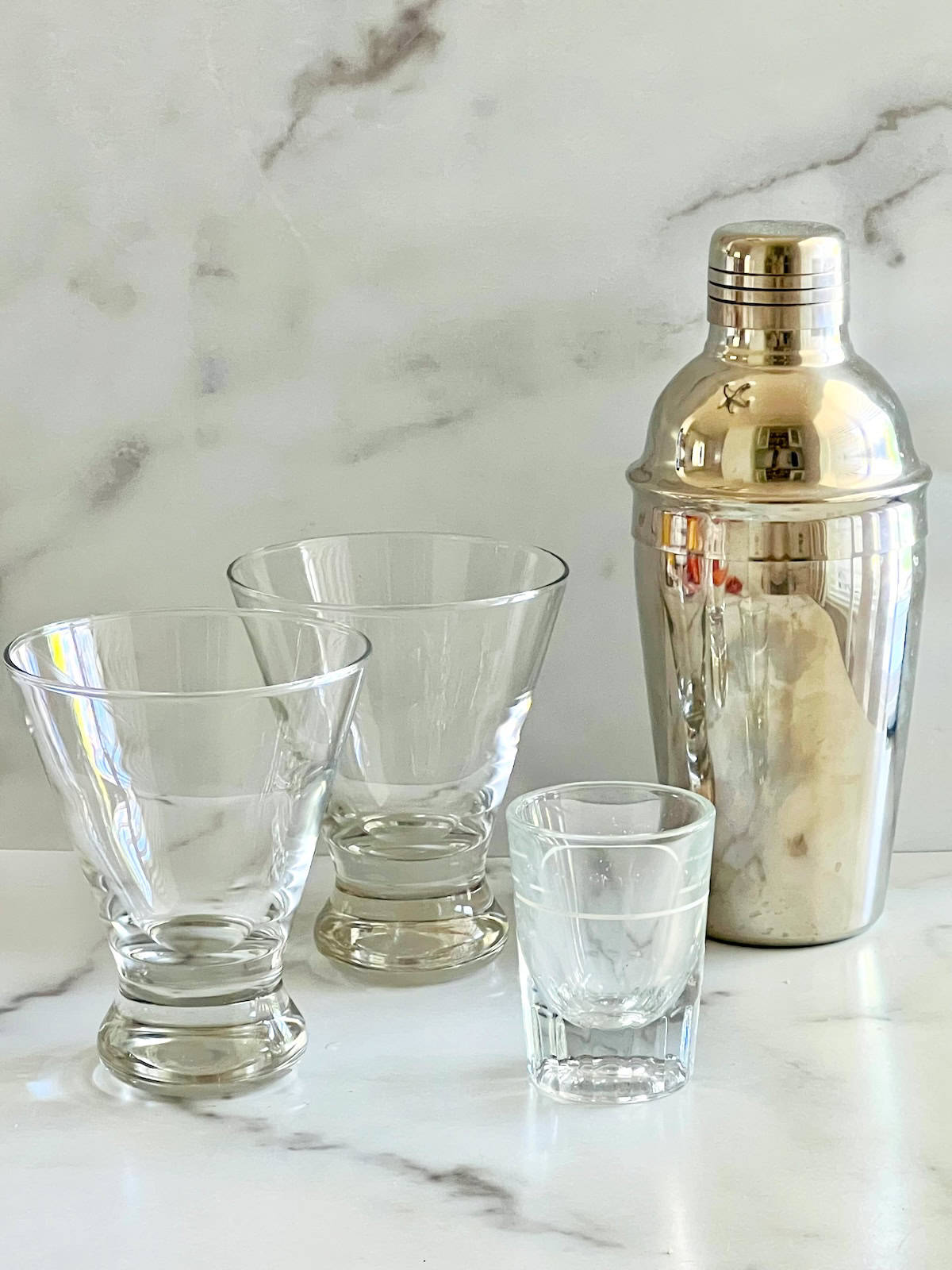 Supplies needed martini glasses cocktail shaker and shot glass on a table.