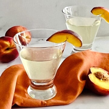 Peach Martini in two glasses with peach slice on the rim.