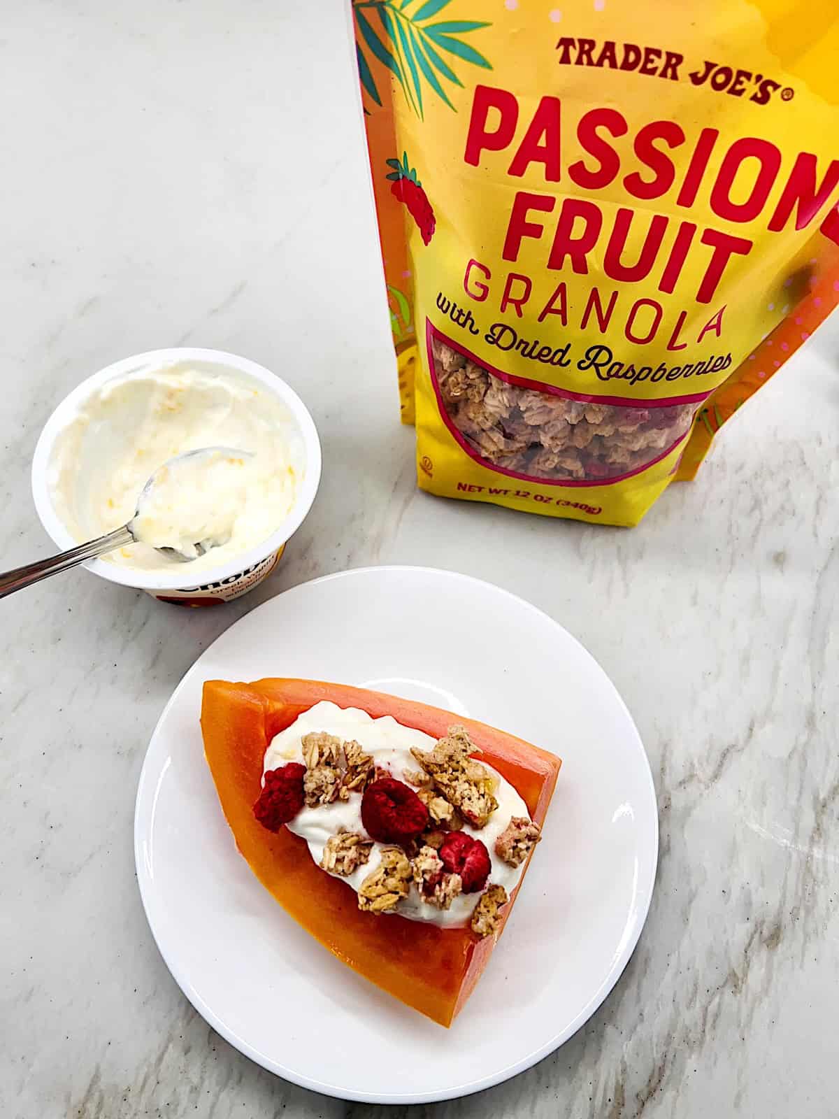 Papaya Yogurt Boats Plated with bag of granola and yogurt cup nearby.