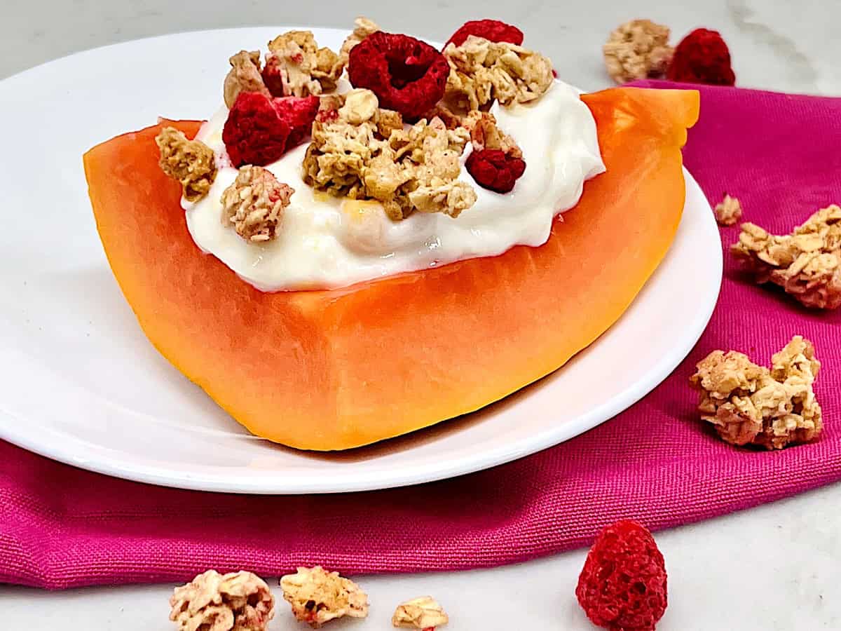 Plate with a wedge of fresh papaya topped with yogurt and granola shaped like a boat.