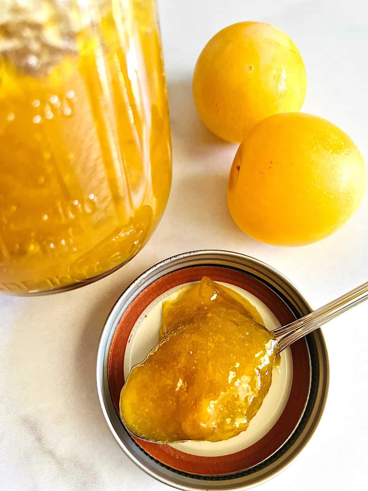 Plum Jam Best recipe spoonful next to mason jar full and fresh plums.